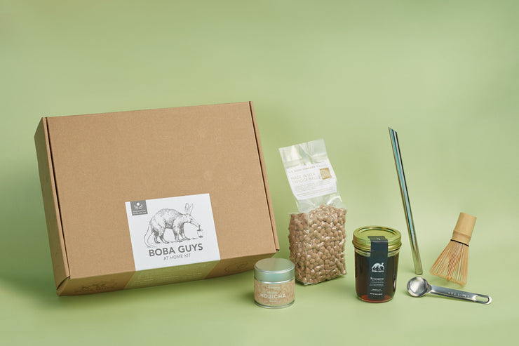 Brown box with 1 lb bag of boba, a Hojicha tea tin, kuromitsu syrup in a jar, a metal straw, a matcha whisk and a metal tea spoon